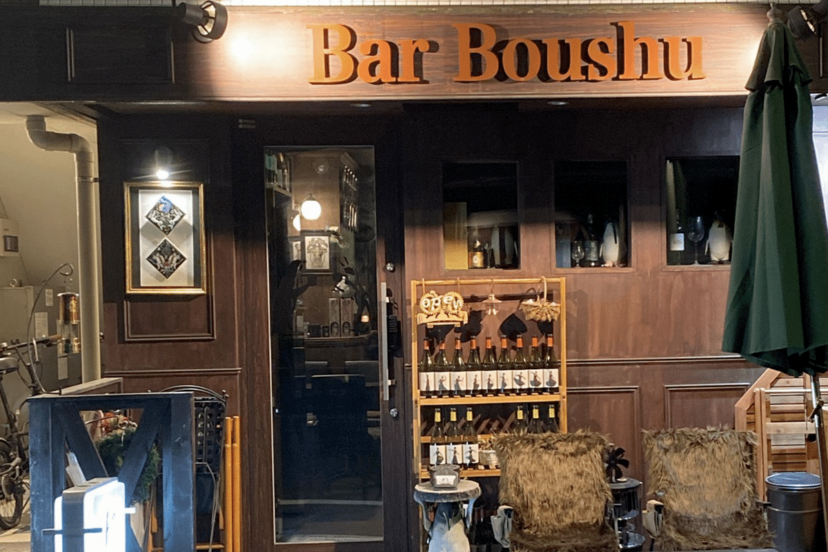 Bar Boushuと書かれたバーのダークウッドのファサードの店構え。表にはワインの瓶、店外用の座席が出されている。