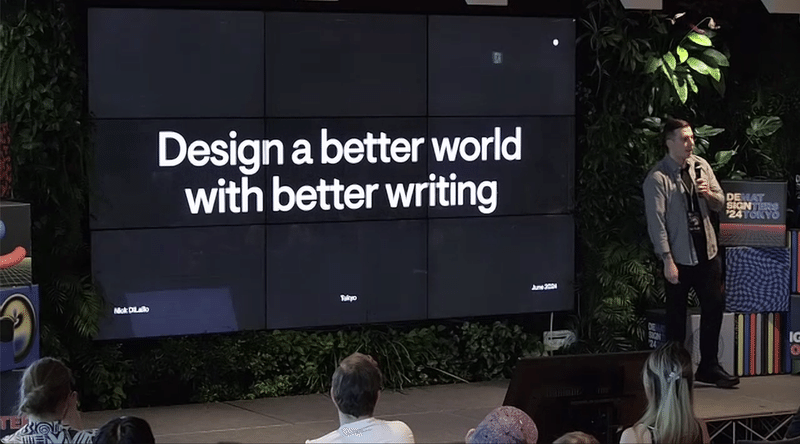 「Design a better world with better writing」と書かれたスライドの前にNickさんが立っている