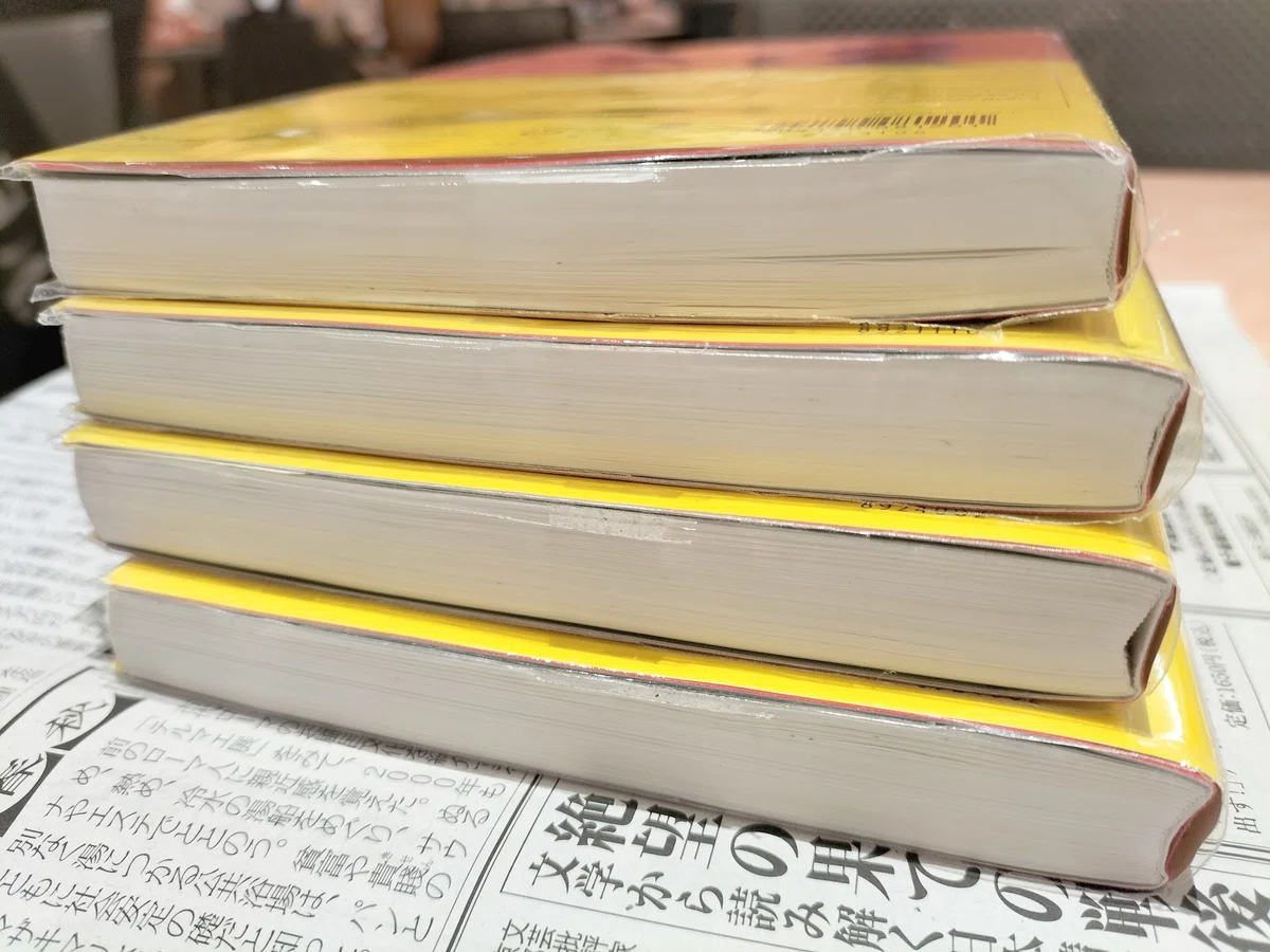 新聞の上に、4冊の赤いノート。1冊の厚さは1cmちょっと。365ページ書ける方眼タイプ。B6サイズ。手帳用紙なので軽くて持ち運びやすい