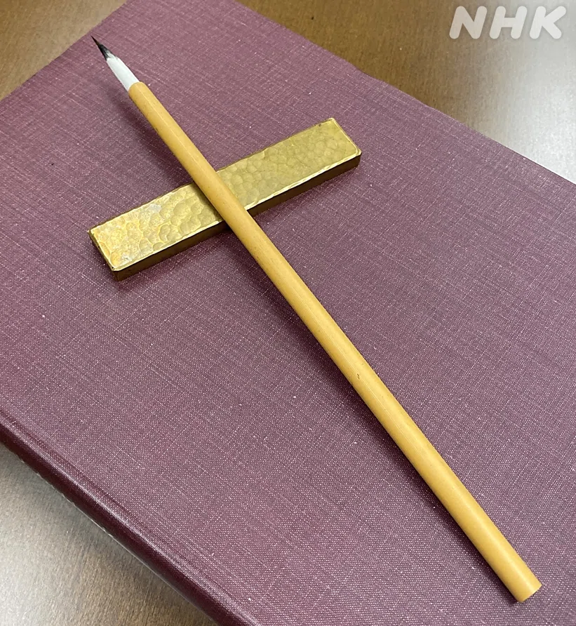 文鎮の上に小筆が置いてある。根元は白く、スッと伸びた穂先だけが黒い。