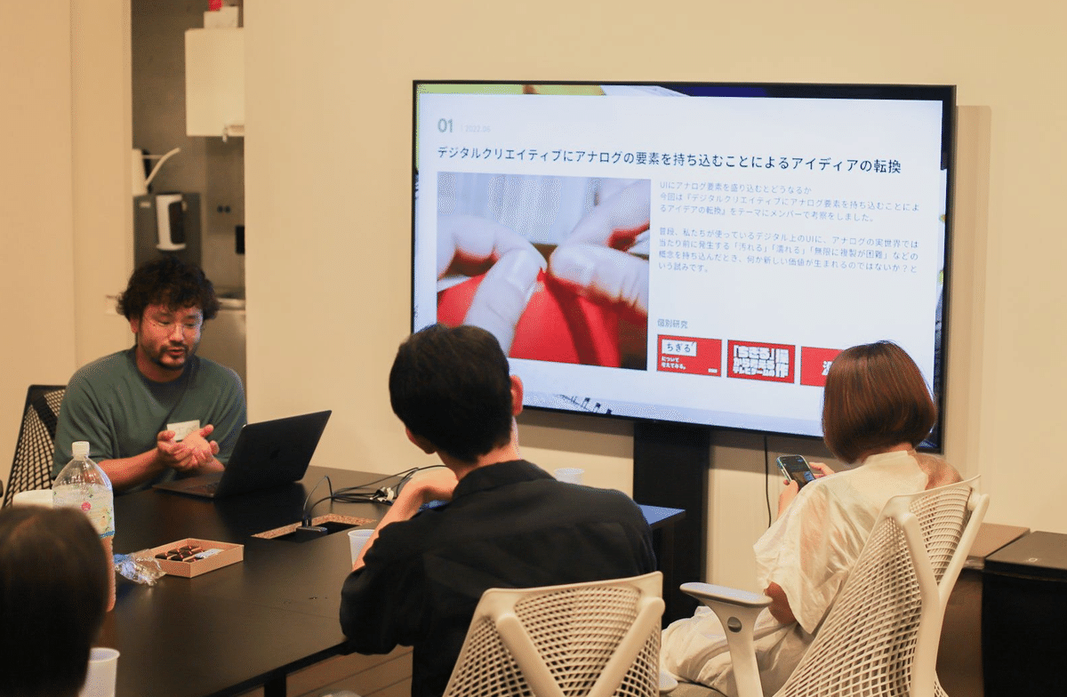 写真。登壇者の江辺さんが身振りを交えつつ、スライドを使って「デジタルクリエイティブにアナログの要素を持ち込むことによるアイディアの転換」について説明している様子。