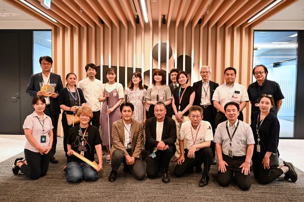 日本IBM×ココテープWORKSHOPの集合写真。ワークショップ参加者、視覚障害リードユーザーなど、総勢18名が笑顔で前を向いている。