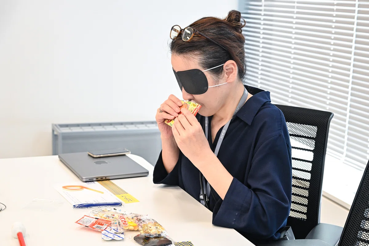 アイマスクを着けて、アンパンマングミの袋の匂いを確認する女性の写真。