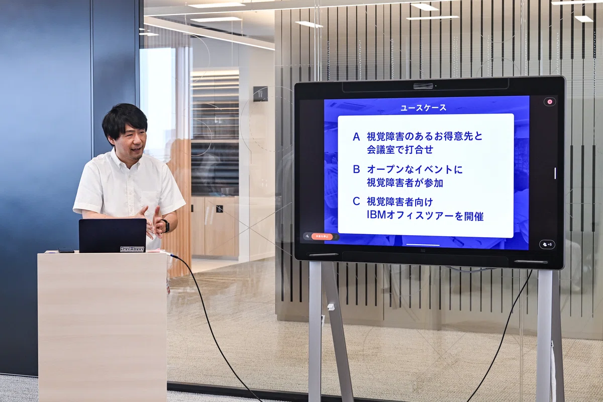 モニターに投影したユースケース３種類の説明をするタキザワ。