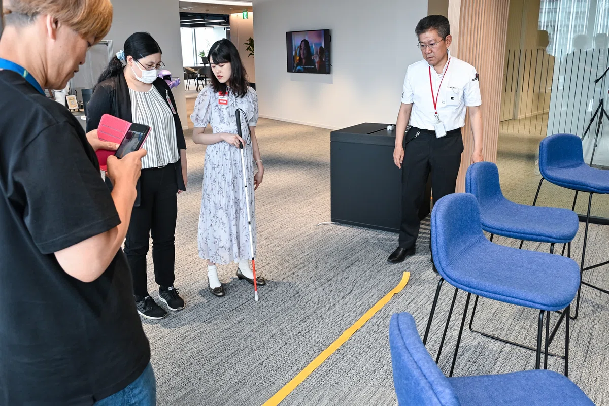 椅子と通路を区切るように設置された長尺のココテープを囲み、意見を交わす参加者の写真