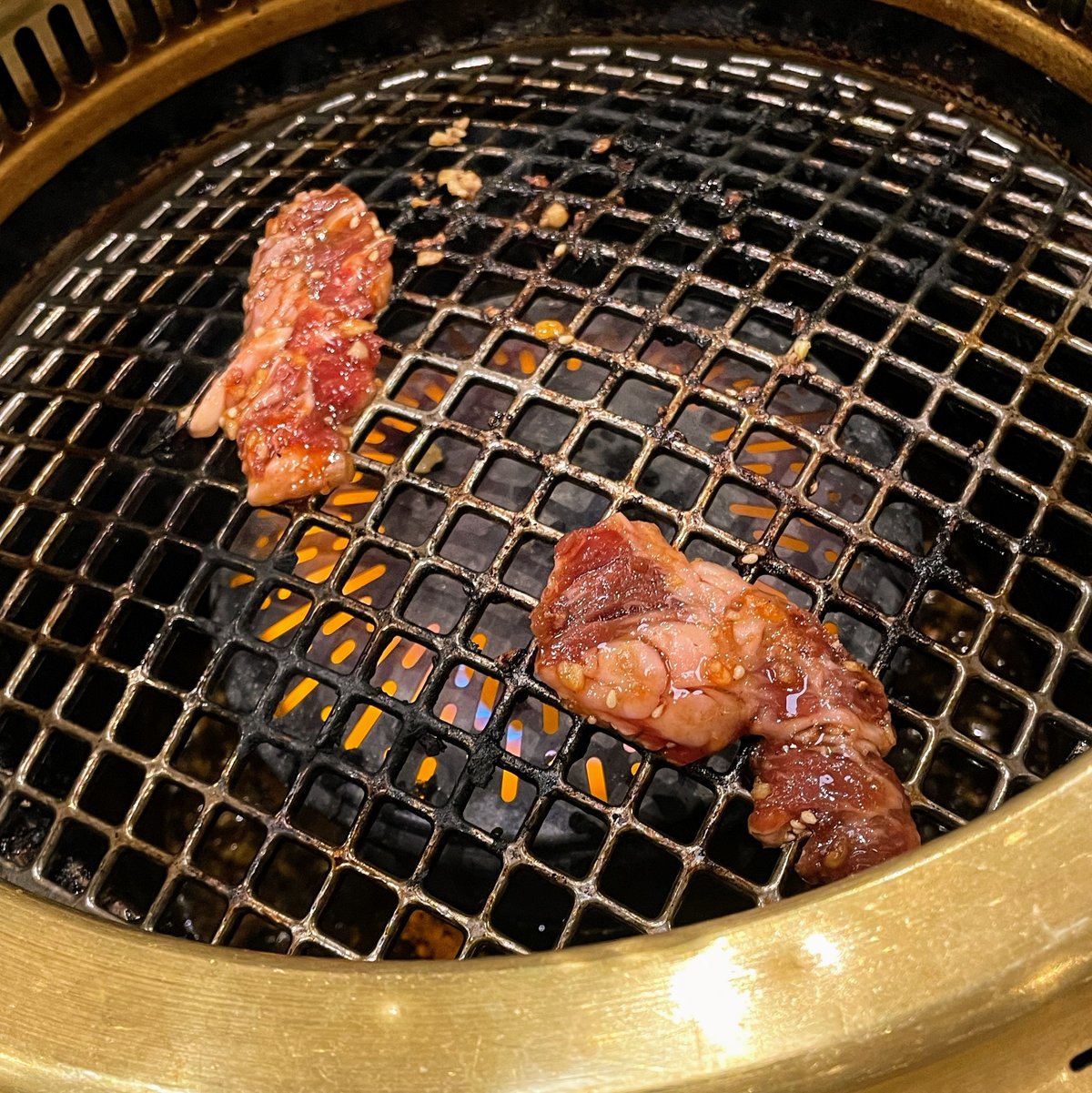 焼肉コンロの網の上で2枚の牛カルビ肉が焼かれている　上面はまだ生