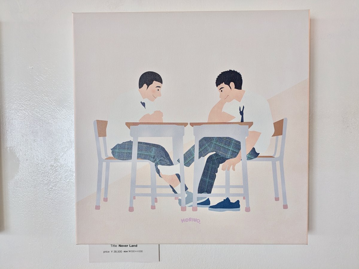 Two young men are sitting facing each other at desks in a classroom. They have taken off their shoes and are stroking each other's feet under the desk.