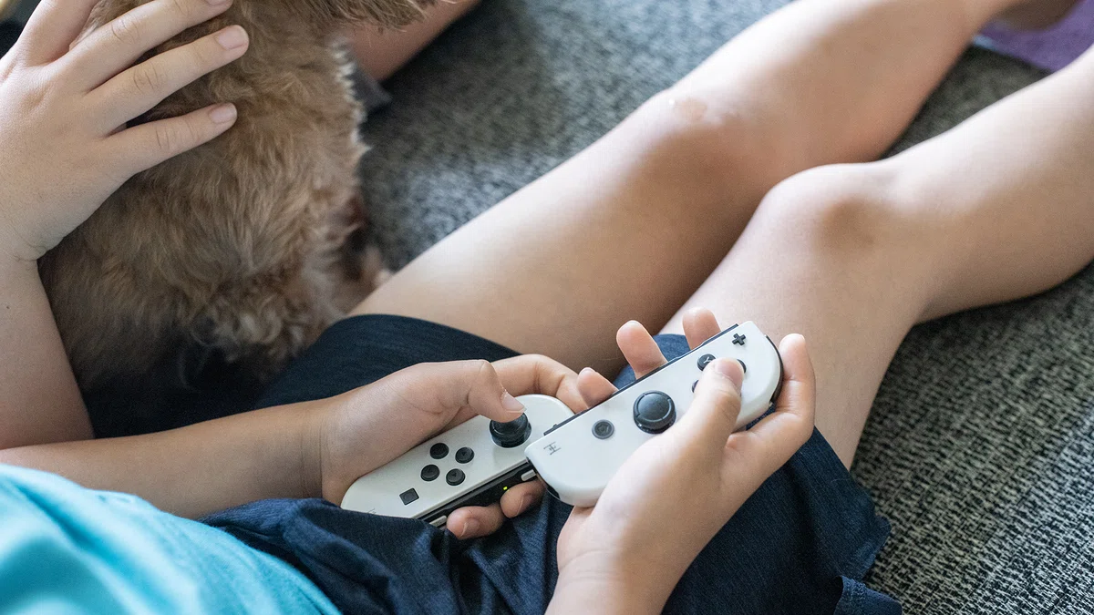 Nintendo SwitchのJoy-Conを操作する小学生と寄り添う犬。ゲームを通じた英語学習やeスポーツ英会話のある日常。