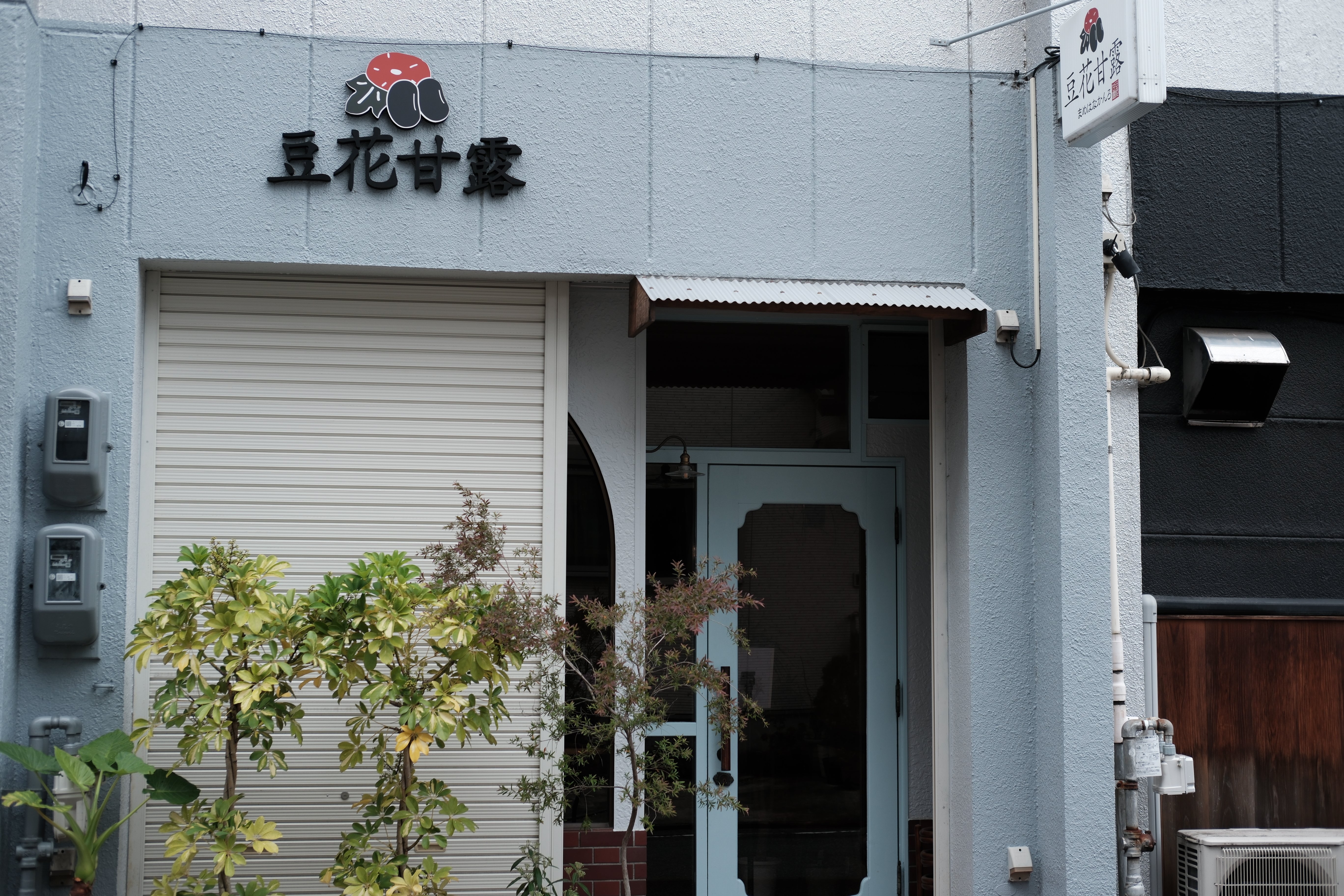 豆花甘露と書かれたお店の外観。壁とドアは落ち着いた水色。開店前、左半分のシャッターがまだ閉じている様子
