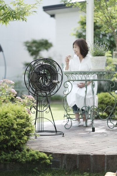 画像上品なガーデンファニチャーに並んでアイアン製のホースリール〈メリー〉が置いてある風景