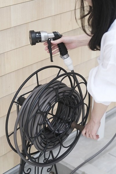 画像白いシャツの女性がお庭のホースを巻き取っているところ