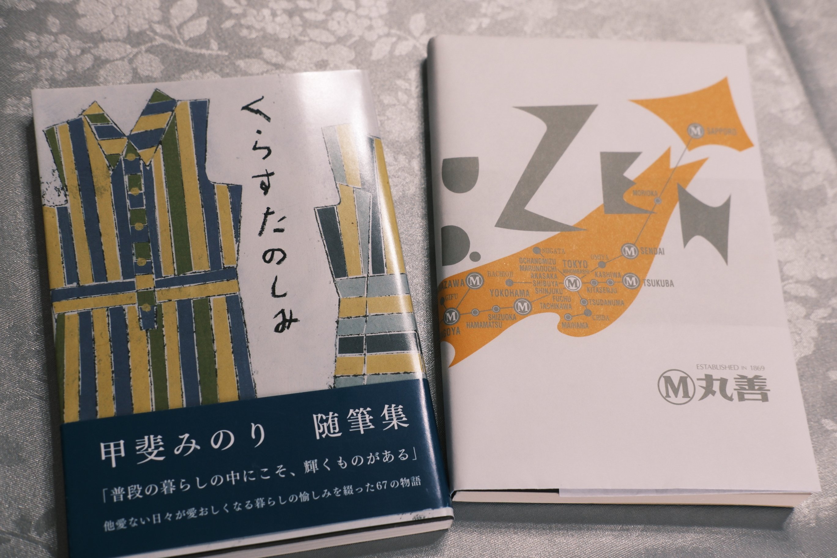 ２冊の文庫本。甲斐みのり随筆集、くらすたのしみとたべるたのしみ。片方の本には丸善のブックカバーがかけられている
