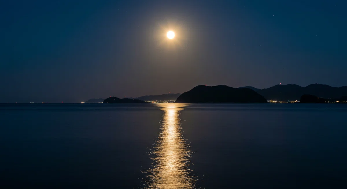 静かな水面に月が映り込む、情緒的で美しい夜の海の風景。