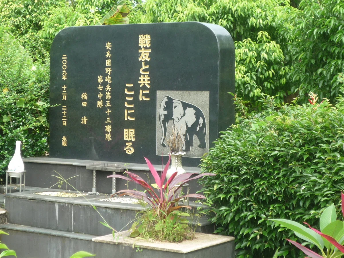 「戦友と共にここに眠る」の金文字と象のレリーフ。香炉が置かれた黒い碑。