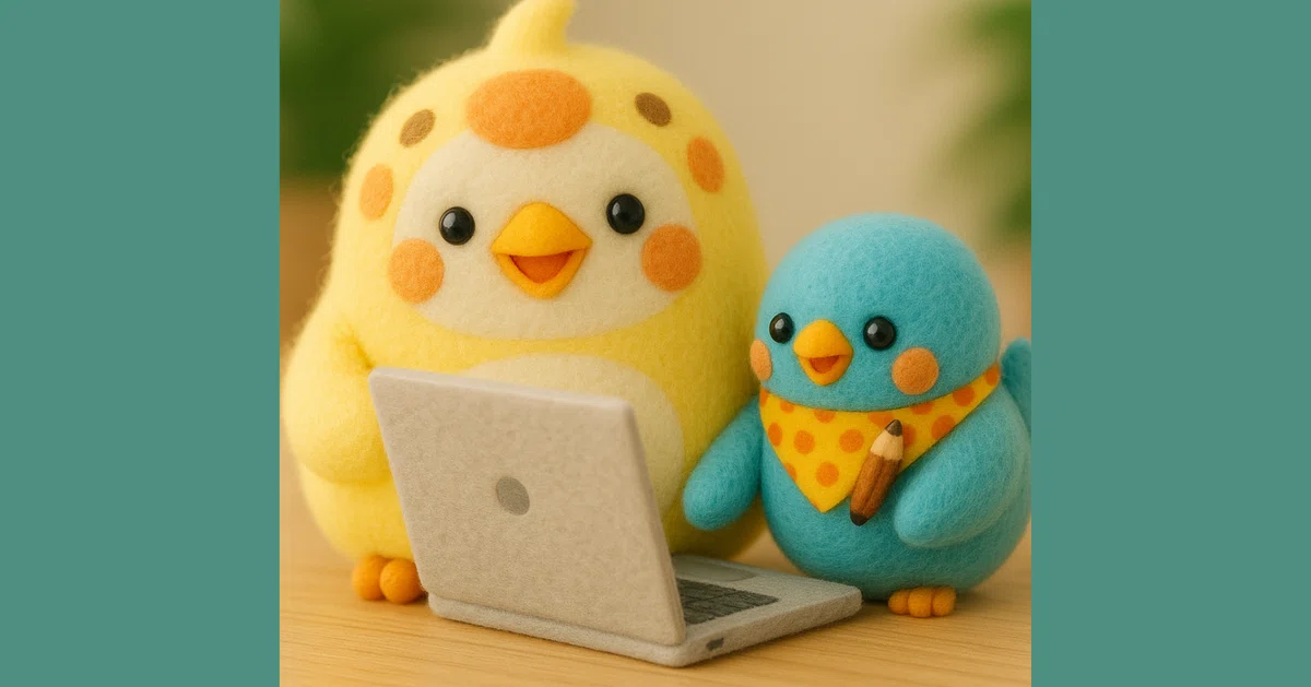 羊毛フェルトで作られた黄色い鳥のペン吉と、青い鳥のことりさんが机の上に並んで座り、ノートパソコンを一緒にのぞき込んでいる。ペン吉は大きな瞳でにっこり笑い、ことりさんはオレンジの水玉スカーフを巻き、小さな鉛筆を持っている。仲良く出版作業をしているような、あたたかく楽しげな雰囲気が漂っている。