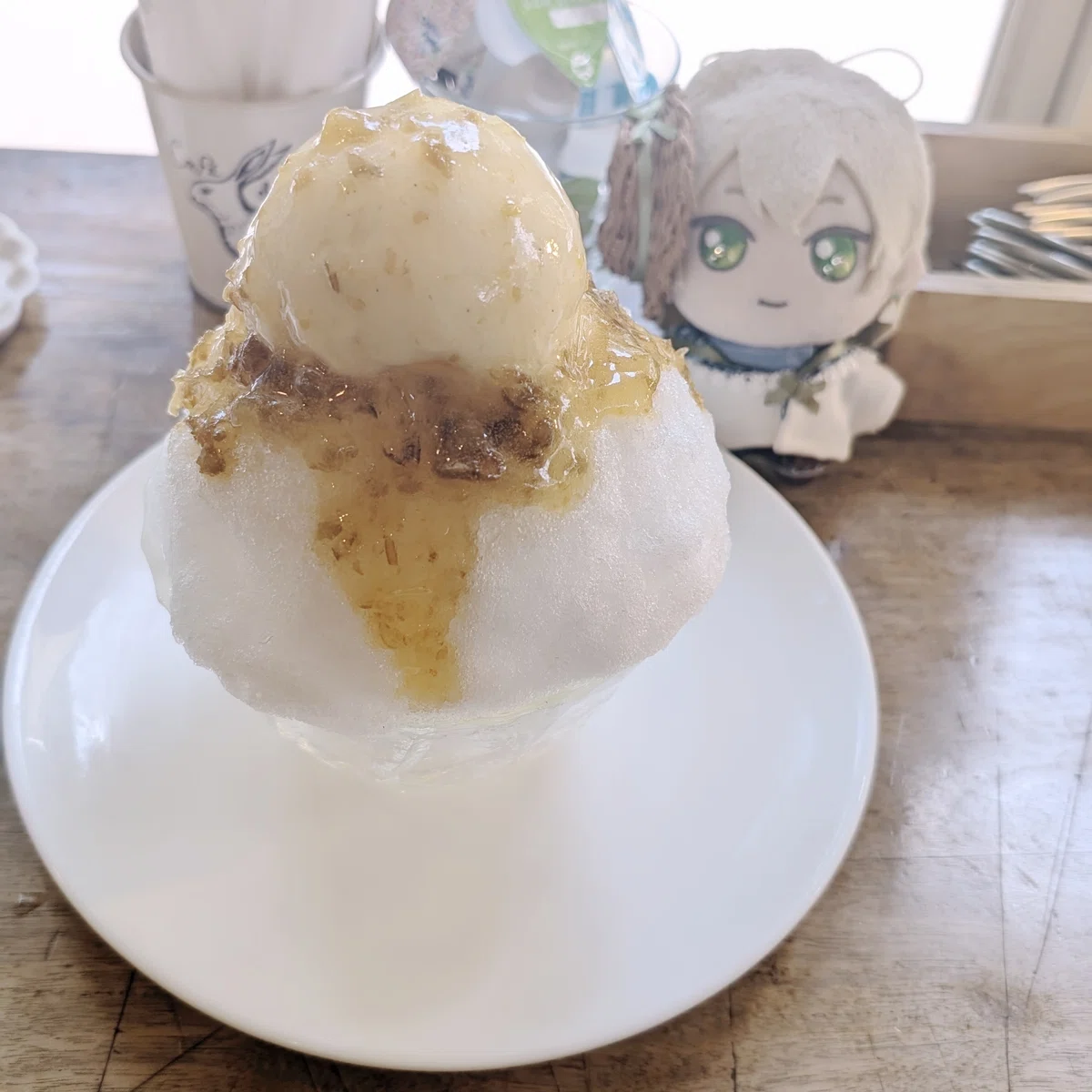 カフェのテーブルに置かれたかき氷の写真。梅果肉のはいった梅シロップとアイスクリームが上に乗っている。