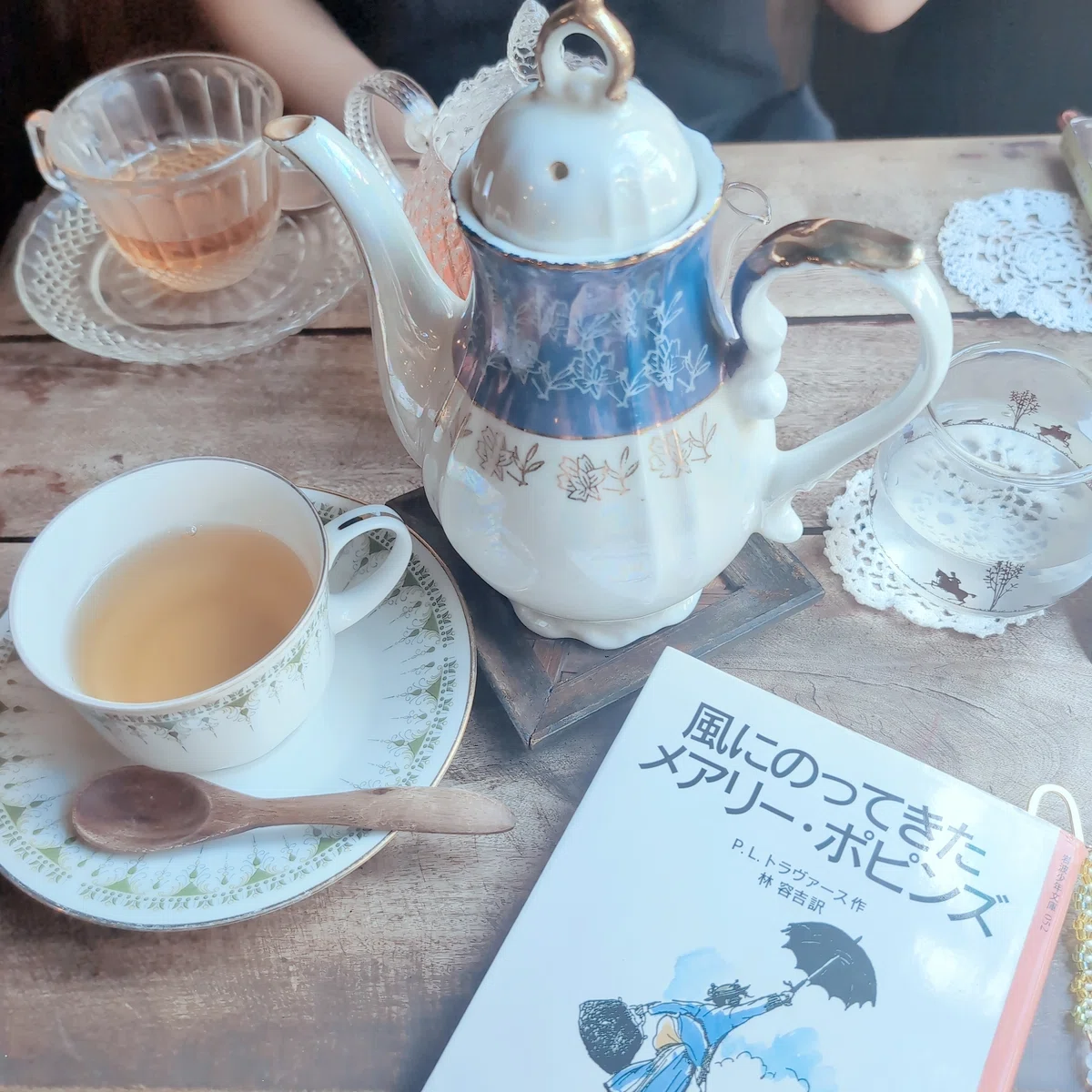 カフェのテーブル。縦長のポットと紅茶の入ったカップアンドソーサー、風にのってきたメアリーポピンズが置かれている。