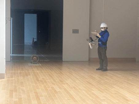 東京都江戸東京博物館内で、通信事業者の専門作業員（白いヘルメットを被り、上着に青色の作業着を着ている）が、機器を操作しながら電波測定の結果を記録している様子。