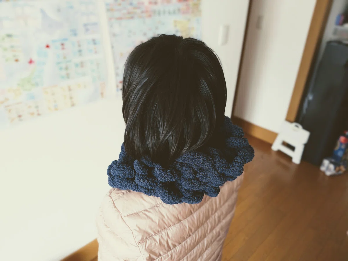 ピンクのダウンをきた少女の後ろ姿。首にネックウォーマーをつけている。ネックウォーマーというより、エリザベスカラーになってしまった