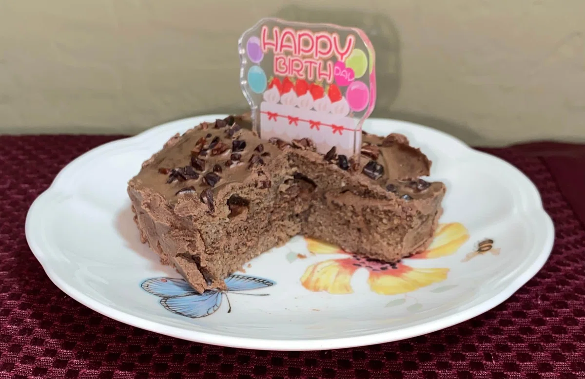 アイシングが塗られたプロテイン入り手作りミニチョコレートレイヤーケーキの写真。ミニケーキの上にはダイソーの誕生日アクリルスタンドを飾り、レイヤーが見えるようにカットしています。