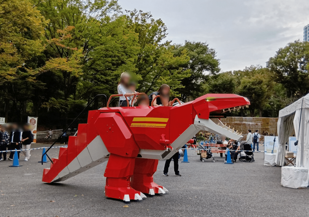 新宿中央公園にて、親子が恐竜型ロボット(赤)を操縦する様子。