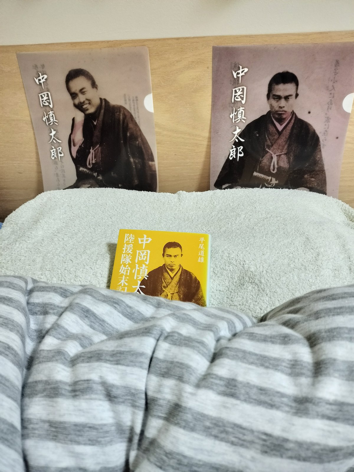 枕元に置かれている中岡慎太郎のクリアファイル2種類。笑顔と真剣な顔。枕には「陸援隊始末記」が置いてある。