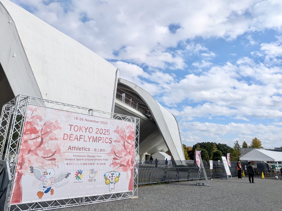 会場のひとつ駒沢公園。青空の下、白い屋根の競技場を背景に、デフリンピックの桜柄の巨大バナーが展示されている。