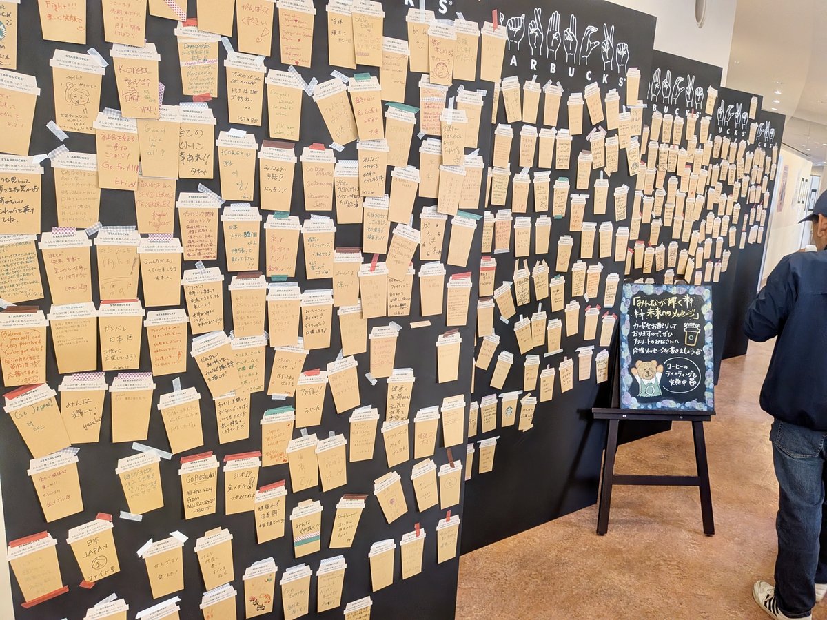カフェスペースの壁。紙コップ型のメッセージカードに、選手たちへの応援メッセージが書かれており壁一杯に張られている。数え切れないほどの数