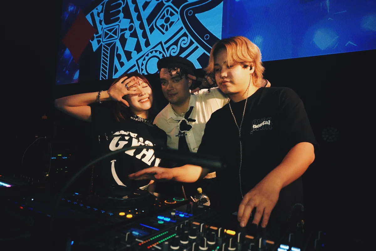 DJブースに3人が並び、笑顔でポーズ。スクリーンにトランプの柄が映り、NESTALらしい華やかな空間を演出。
Three DJs posing together at the booth, with playing-card visuals glowing behind them — capturing the lively vibe of NESTAL at WOMB.