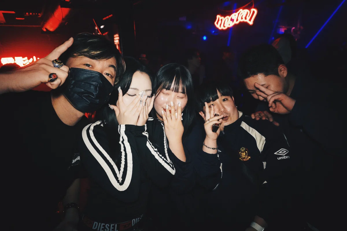 クラブ内でポーズを決めるグループショット。赤い照明と「nestal」ネオンが印象的な、K-POPファンたちの笑顔。
A group of friends posing under the red “nestal” neon sign, radiating the joyful energy of K-POP fans inside the club.