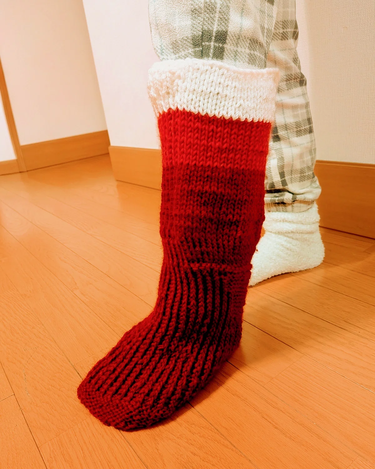 クリスマスのプレゼントを入れる靴下。パジャマ姿の娘が履いている。膝はオフホワイト、膝下はベリーレッド、そこから下つまさきまでワインレッド。目が荒い