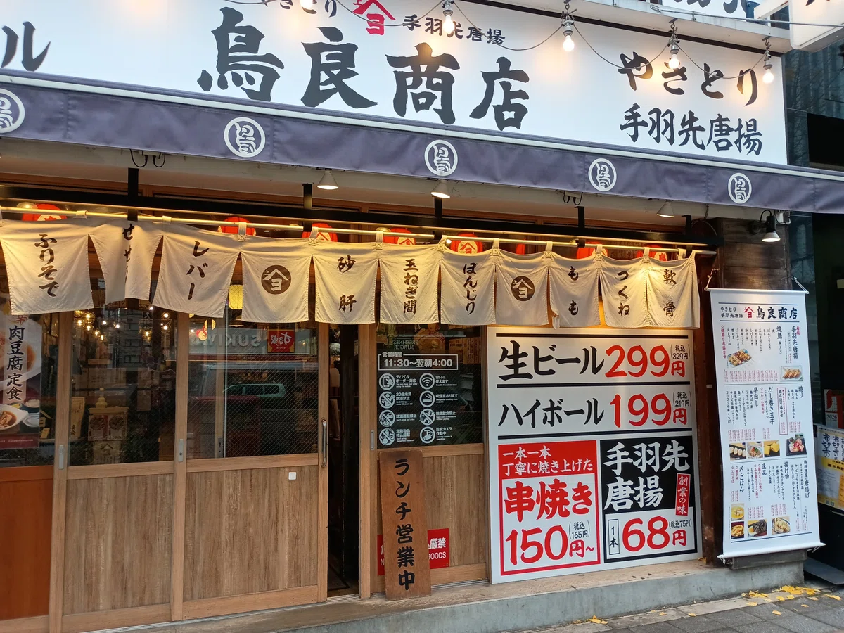 鳥良商店の店頭。のれんが下がり、生ビール299円、ハイボール199円などの価格表示が見える。ランチ営業中の看板も