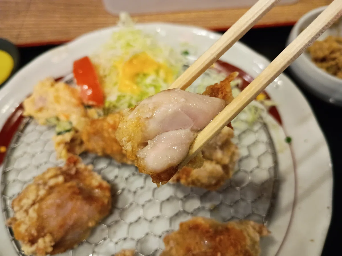 箸で持ち上げた唐揚げの断面。衣はきつね色に揚がり、中の鶏肉はジューシーで白く柔らかそう