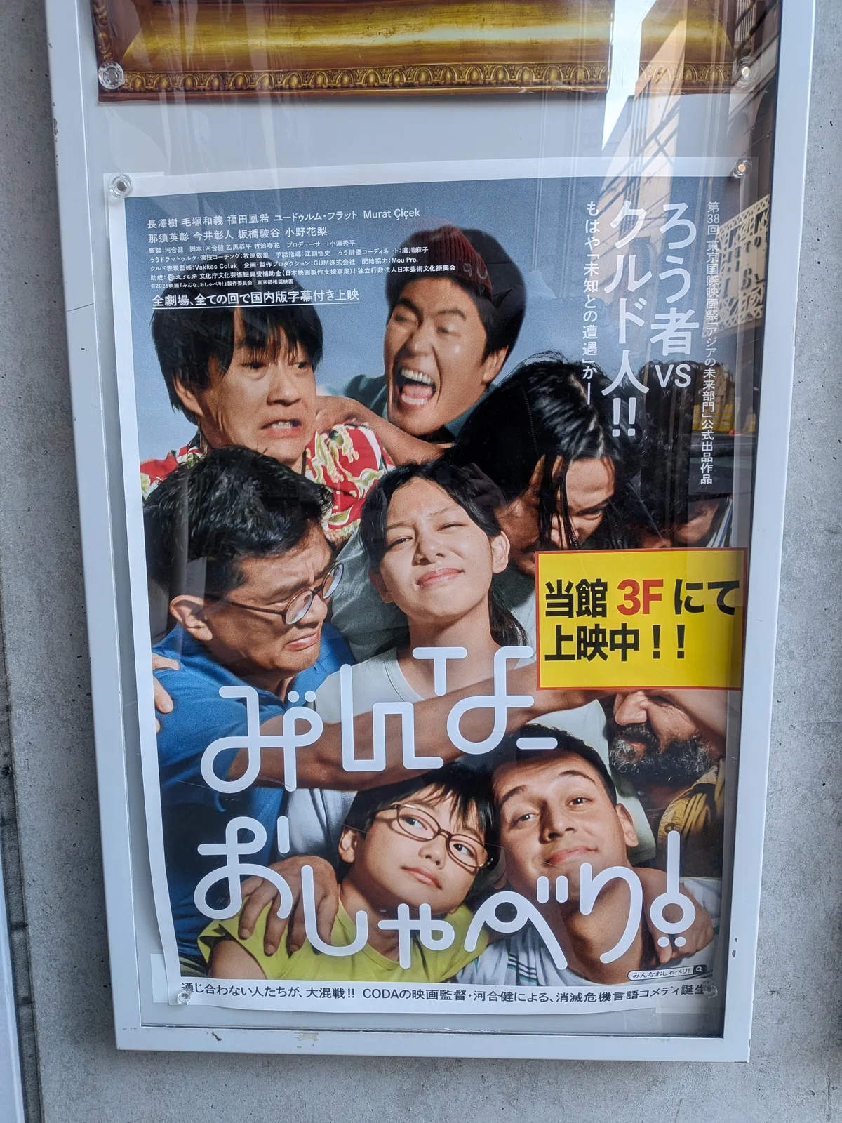 映画のポスター。登場人物たちがとっくみあったり仲良く肩を組んだりしている。中央に主人公が苦笑い。