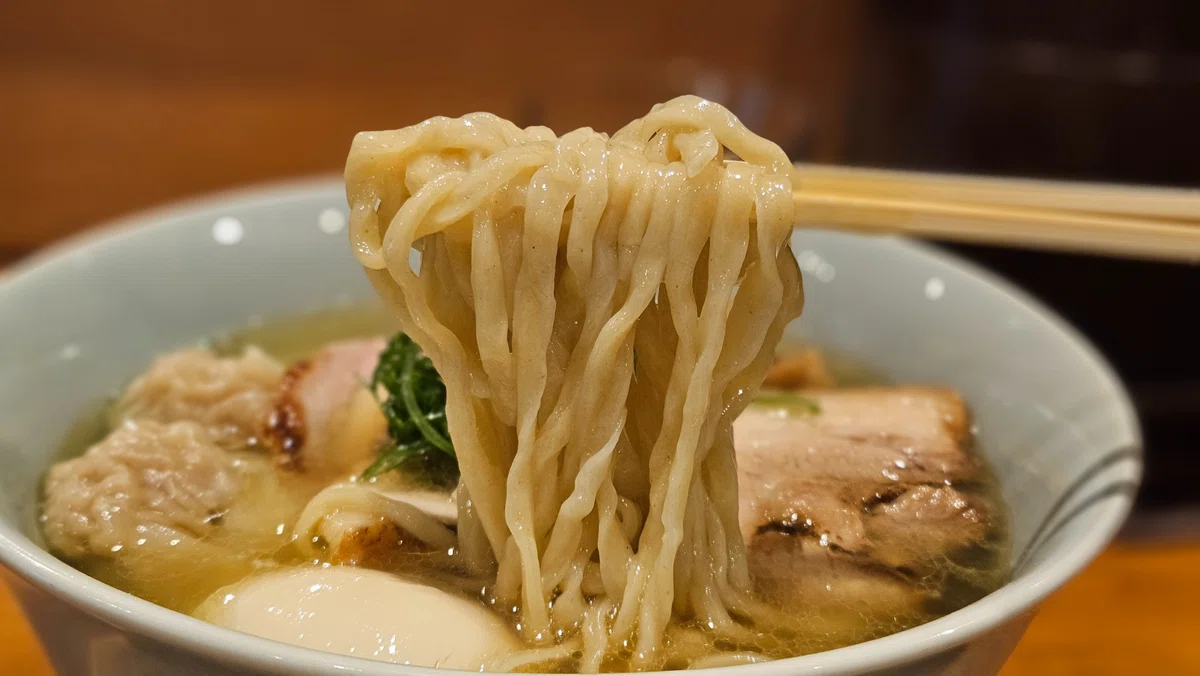 箸で持ち上げた手揉み麺。もちっとしたちぢれ麺が塩スープを絡めている様子。