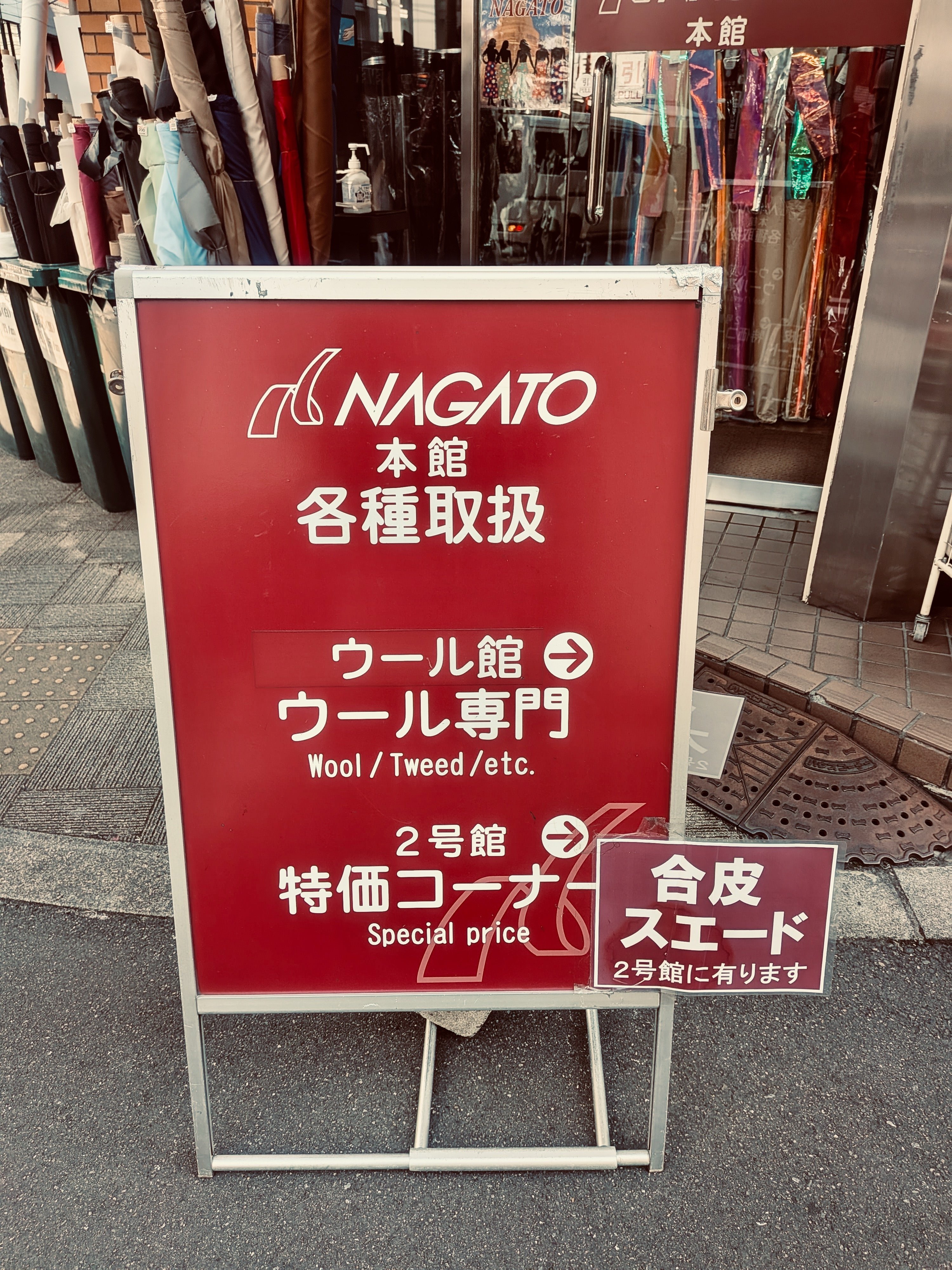 道に置かれた看板。ナガト本館各種取扱　ウール館ウール専門と書かれており、道案内の矢印が描かれている