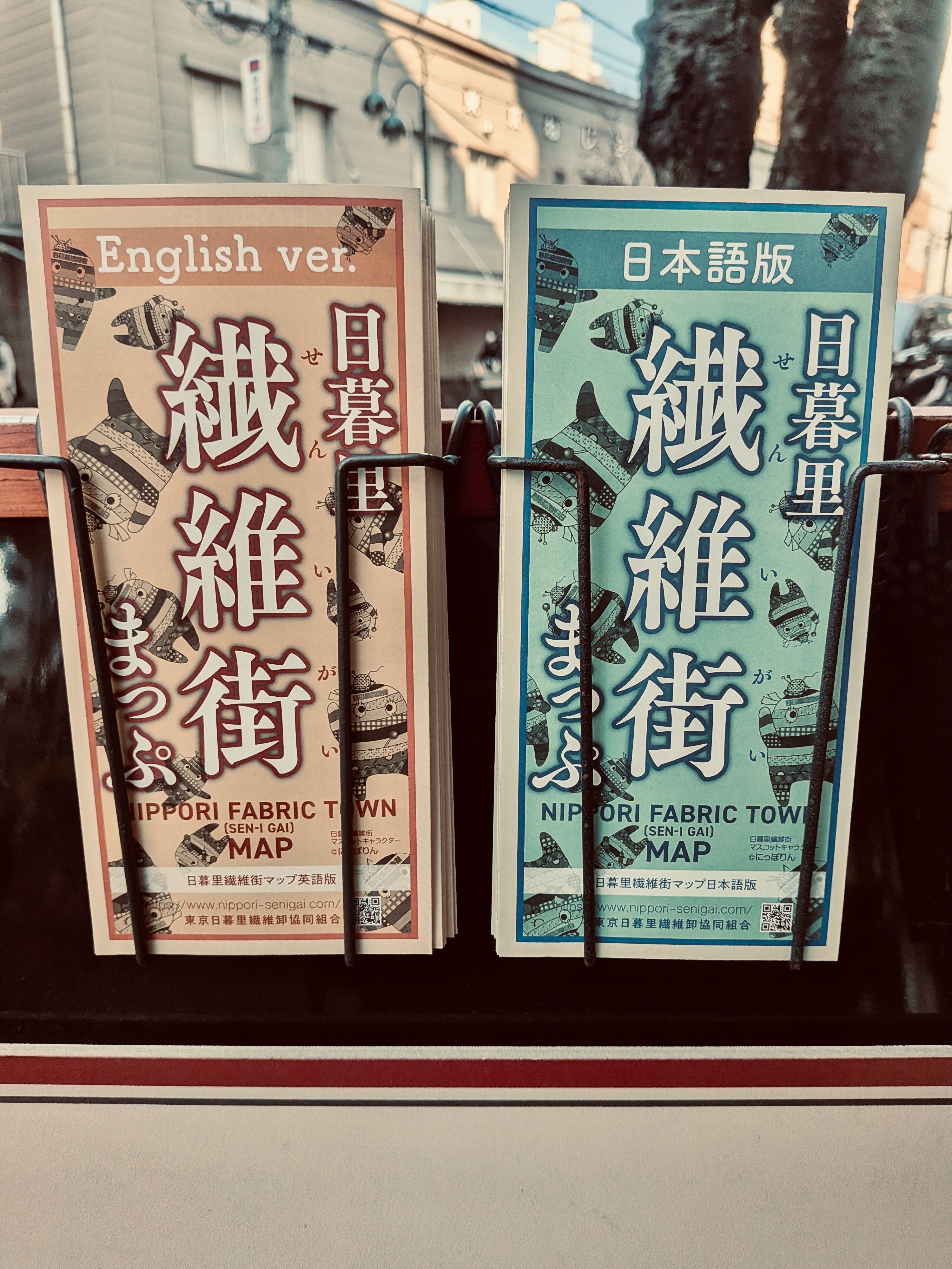 街頭で配られているフリーのタウンガイド。左に赤いデザインで、英語バージョン。右に緑で日本語バージョン。二種類のガイドが並んでいる。