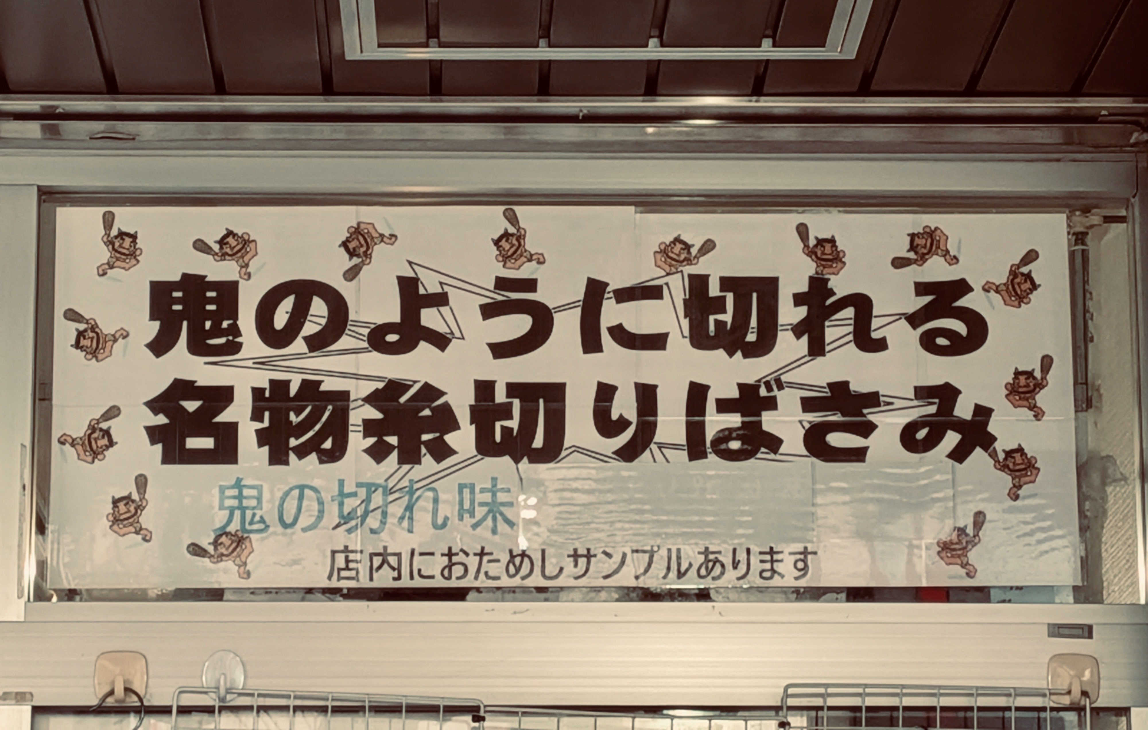 はさみの看板。鬼のように切れる　名物糸切りばさみ　鬼のきれあじ　店内におためしサンプルあります　と書いてある。