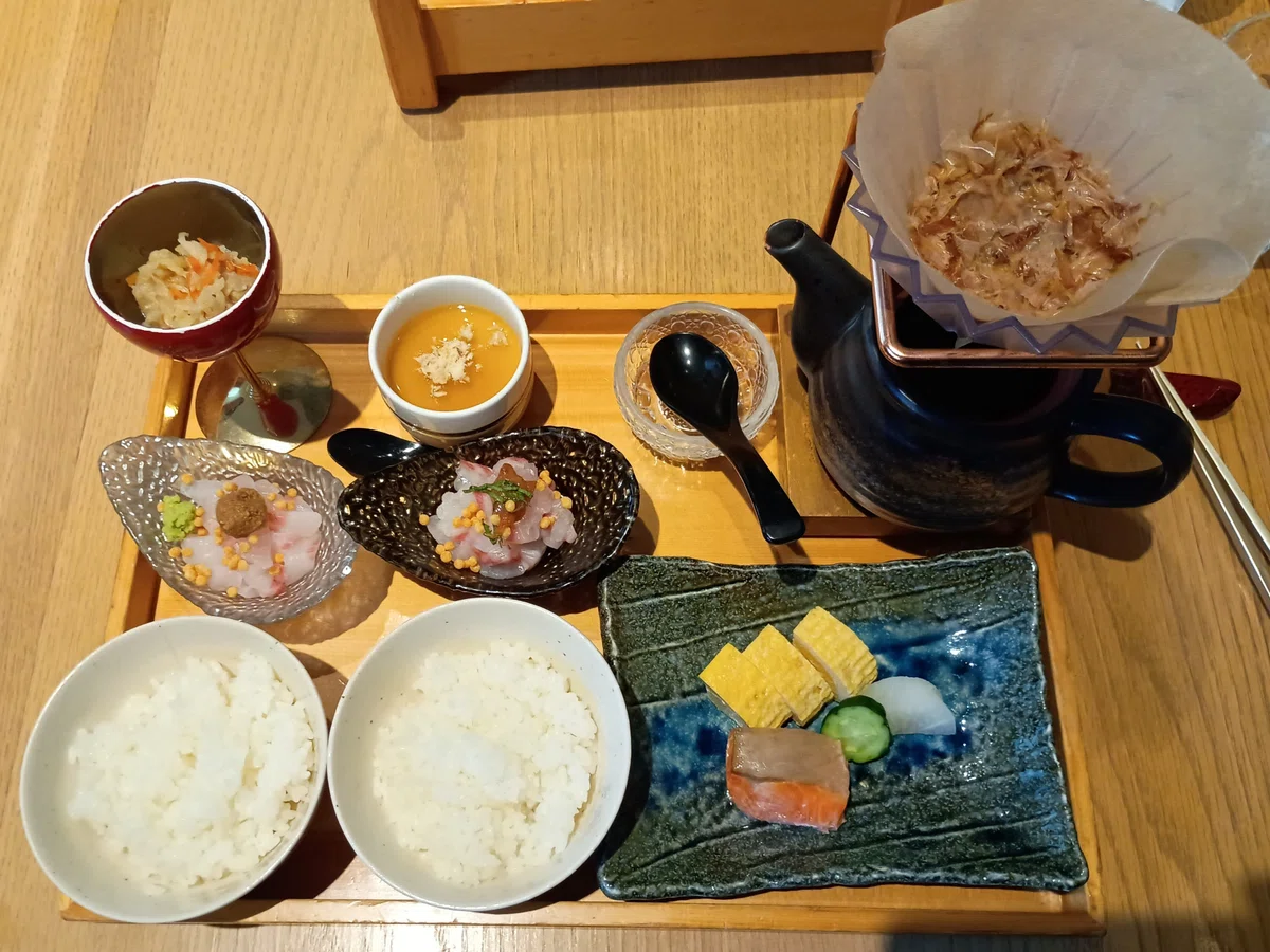 （定食の全体写真）木のお盆に並べられた「SHARI」の鯛茶漬け定食。ゴマと梅の2種類の味付けがされた鯛のお刺身、コーヒードリッパーのような器具で淹れるこだわりの出汁、ご飯、鮭の焼き魚、出汁巻き玉子、茶碗蒸しなどが美しく盛り付けられている。