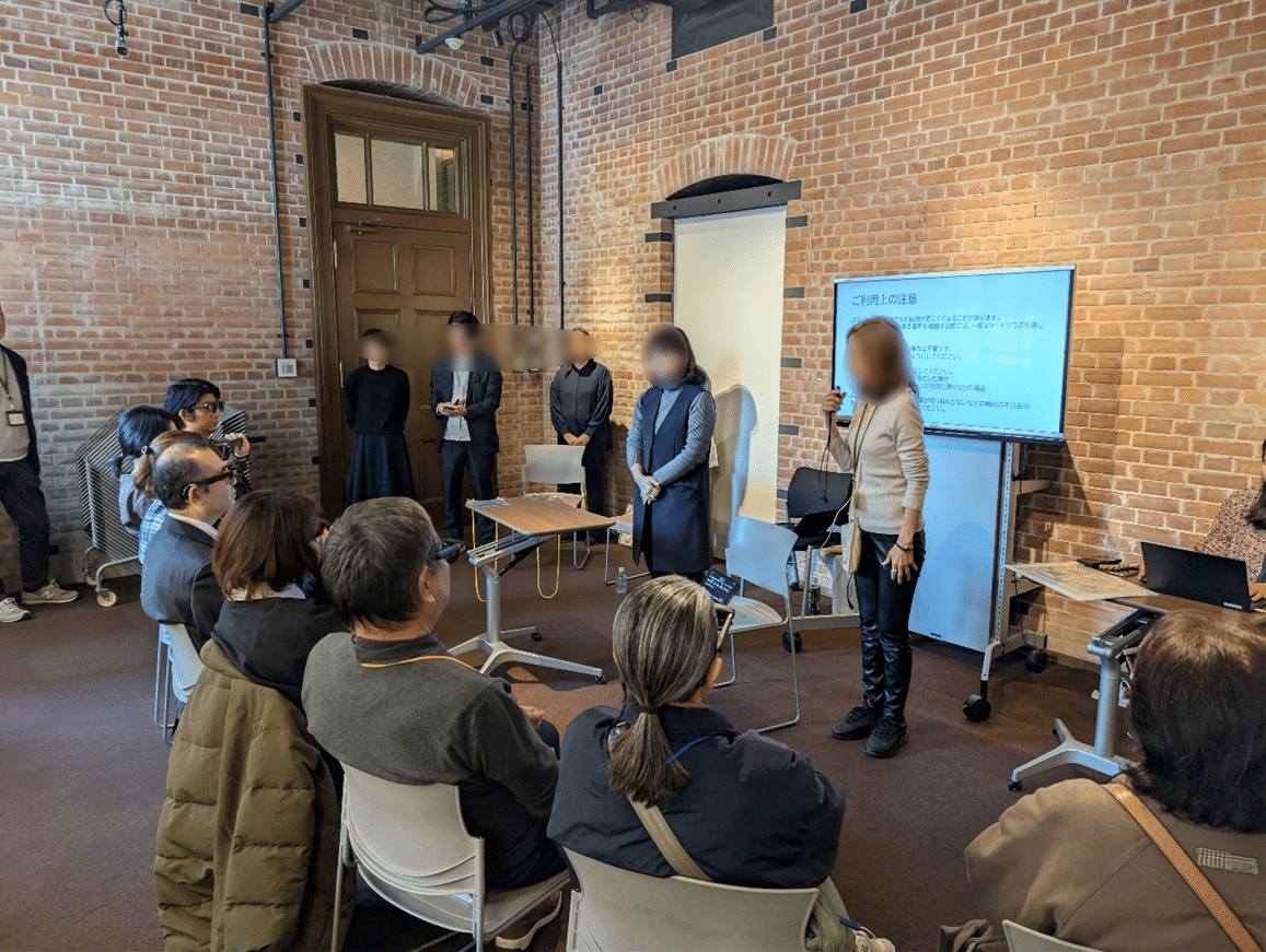 三菱一号館美術館での実証の様子。複数人の聴覚障がいの方がスマートグラスを装着しながら座っており、ガイドからの説明を受けている。