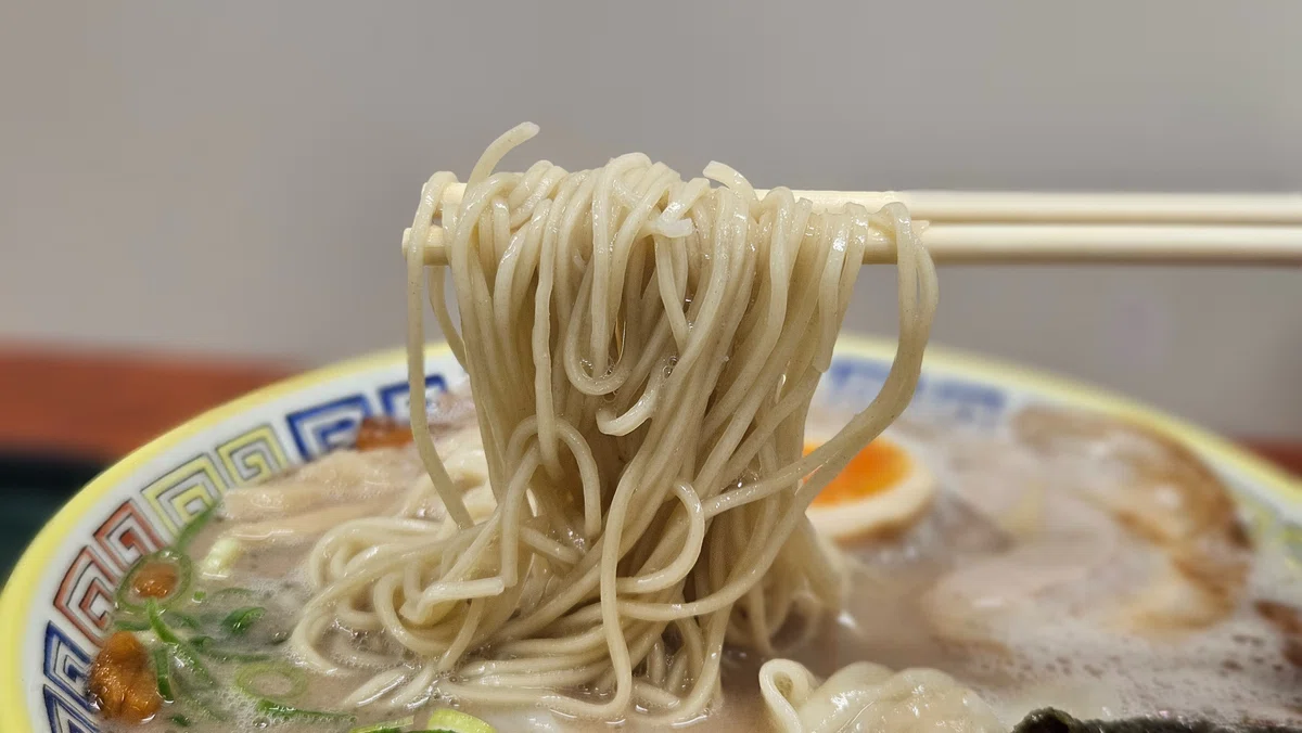 箸で持ち上げた細麺。豚骨スープとしっかり絡む様子がわかる写真