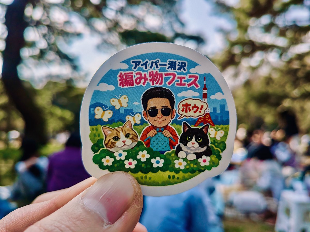 編みフェスのステッカー。アイパー滝沢　編みフェスと書かれている。イラストは、サングラスをかけたアイパー滝沢さんと、猫たち。お花畑で編み物をしている。背景には東京タワー