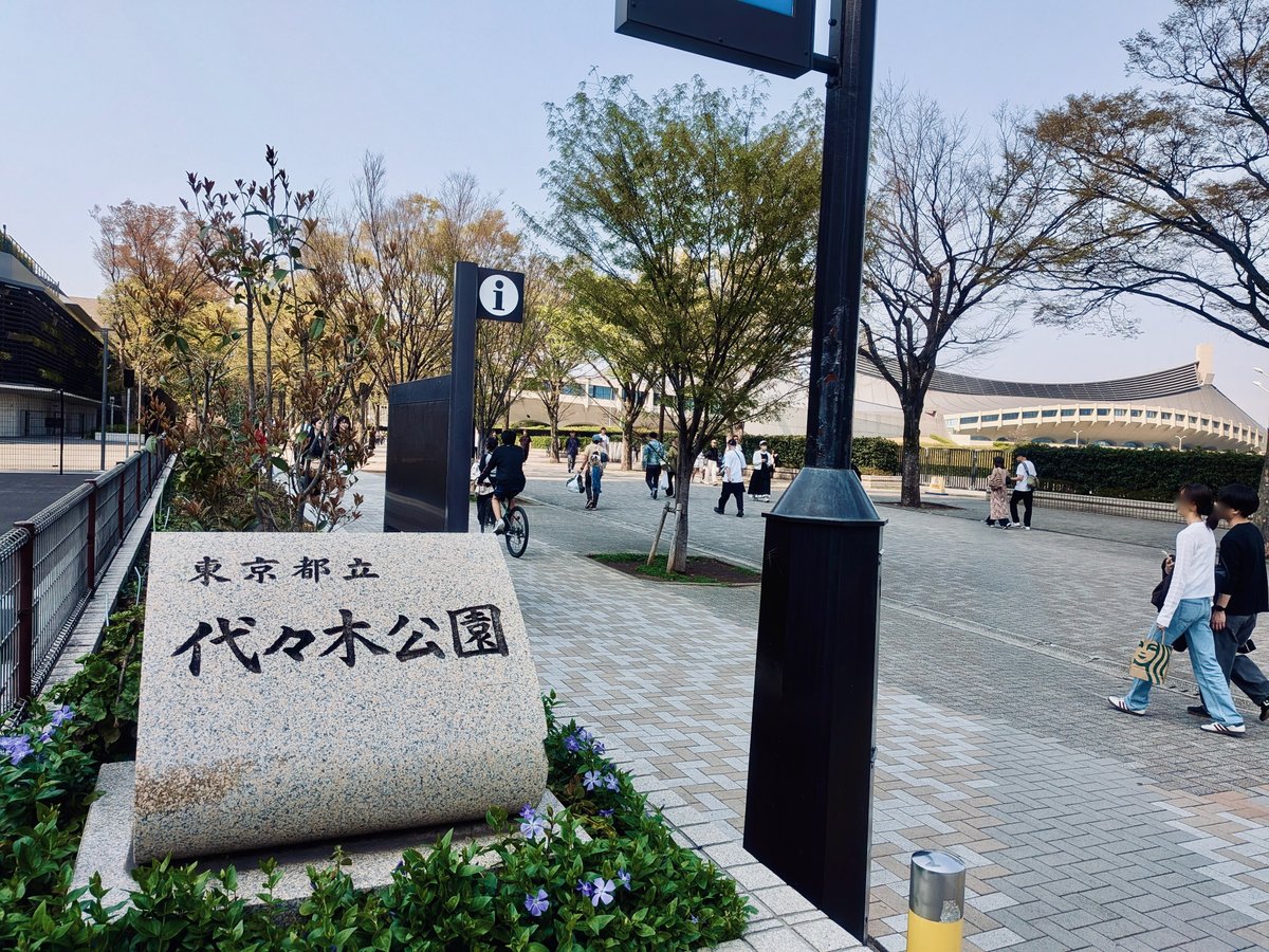 代々木公園の入口。東京都立代々木公園と刻まれた灰色の園銘石。背後には代々木第一体育館が建っている