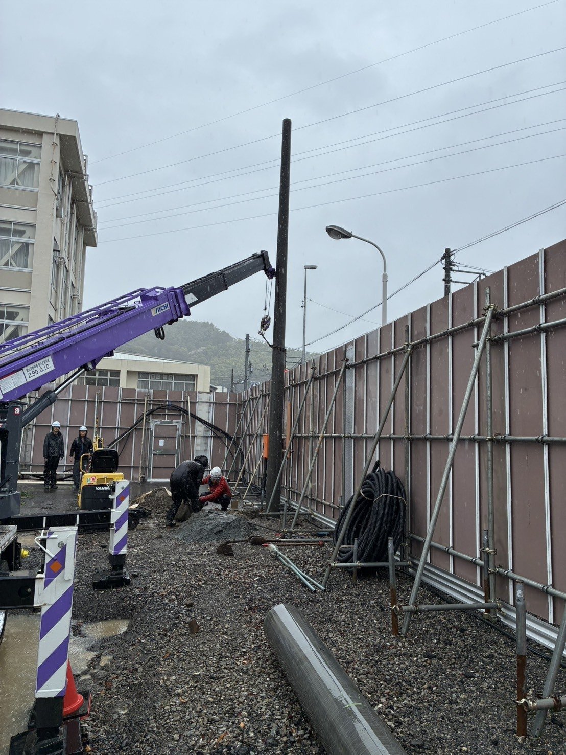 クレーンでコンクリート柱を建てている