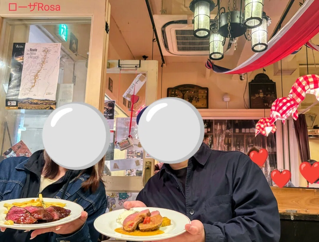 銀座パリのワイン食堂の中でお肉料理を持ちカメラにポーズをする男女の画像