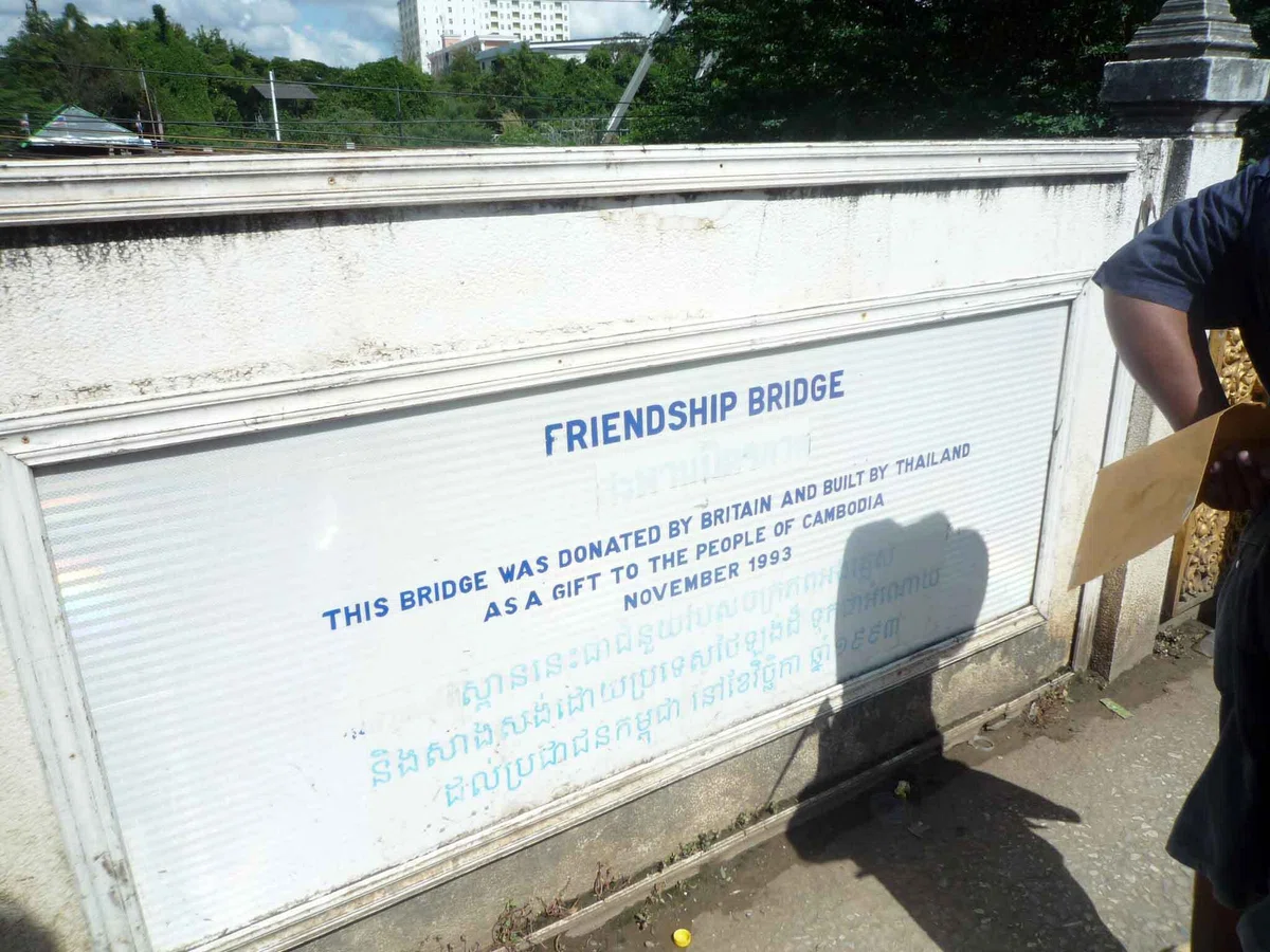 白い壁に “FRIENDSHIP BRIDGE” と書かれた銘板があり、その下に英語とカンボジア語の文字が見える。