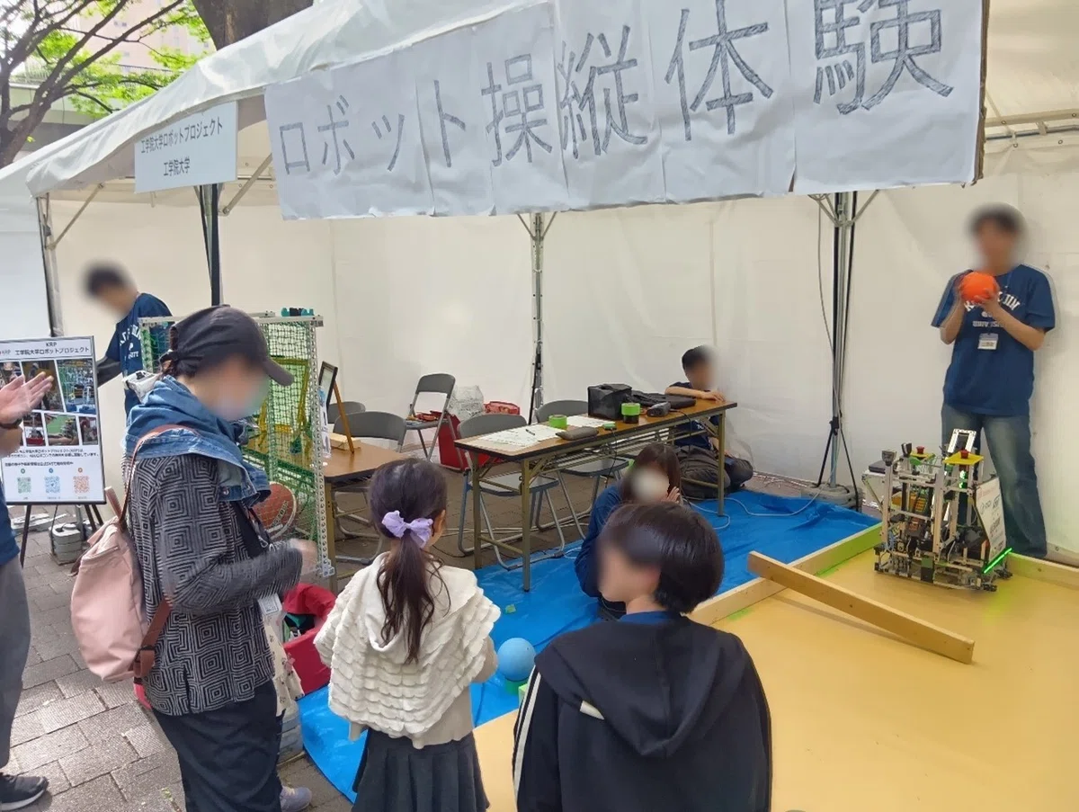 地元大学の学生がフォーミュラカーについて説明し、来場者が車両に乗り込みながら聞いている