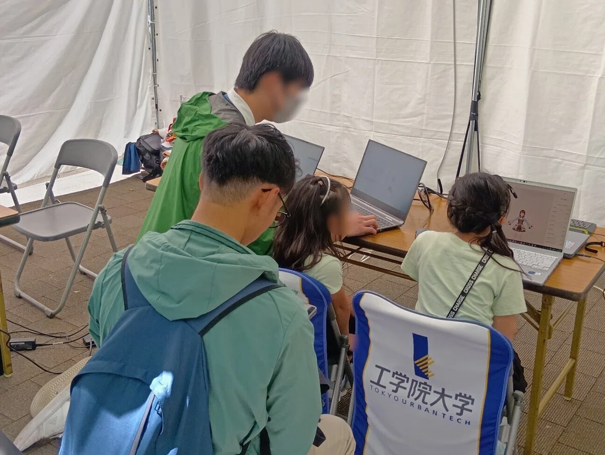 地元大学の学生がフォーミュラカーについて説明し、来場者が車両に乗り込みながら聞いている