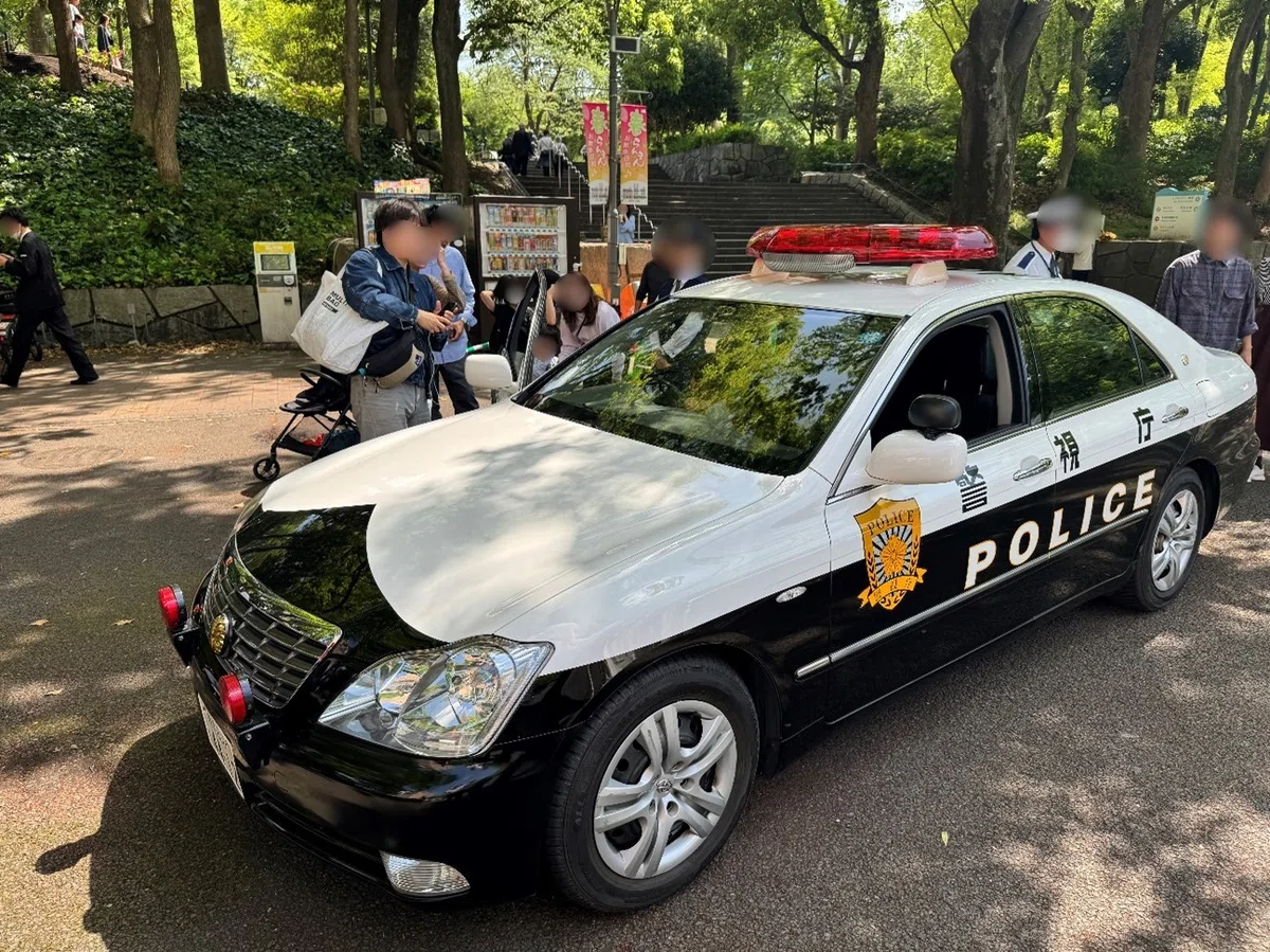 パトカー乗車体験の様子。子供がパトカーの運転席にのり、父親が写真を撮影している。