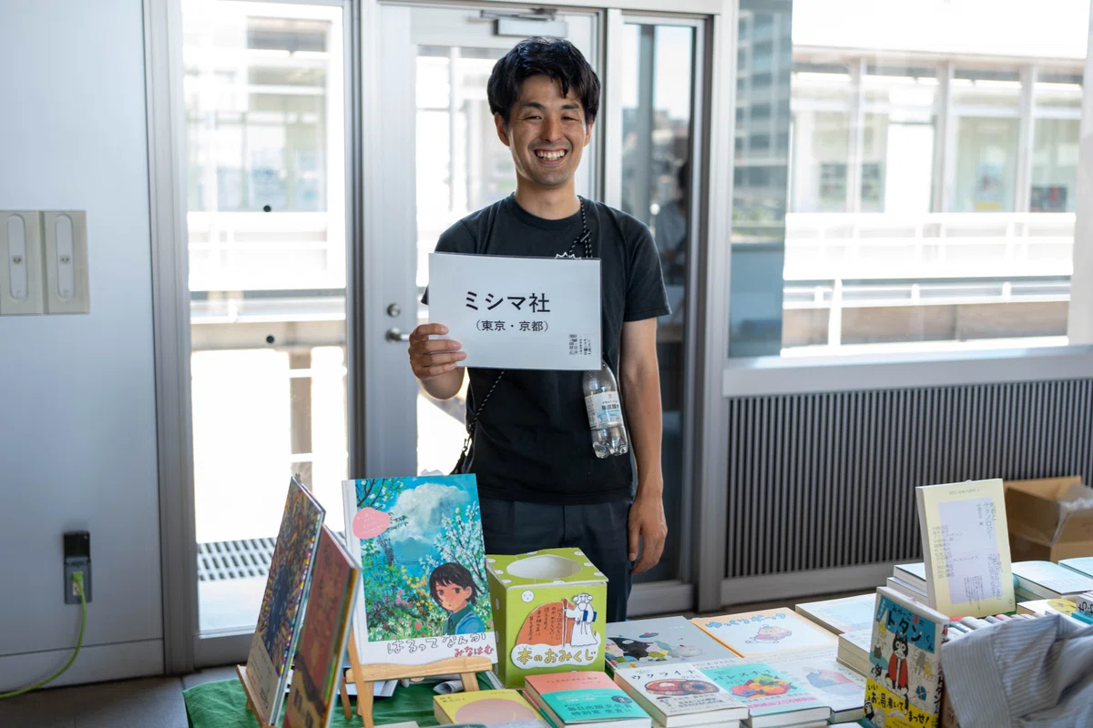 「ミシマ社」の札を持つ笑顔の男性
